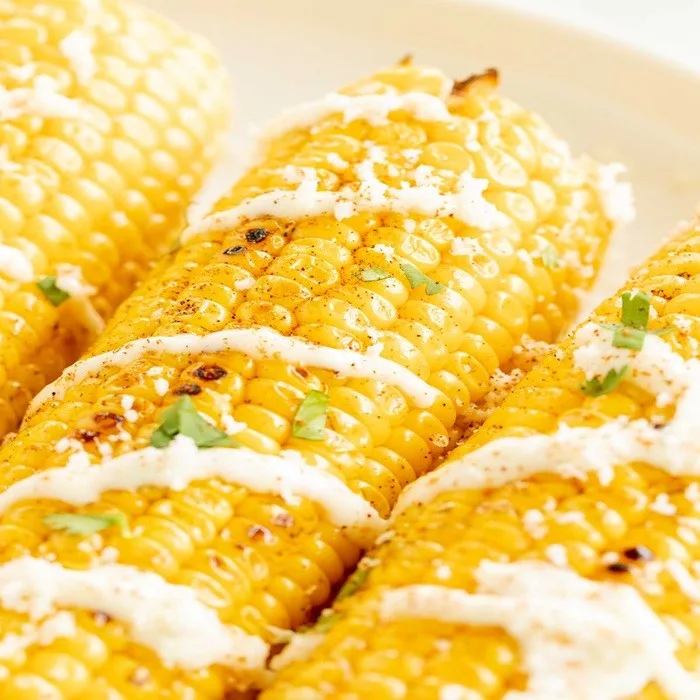 Gegrilde maïs met knoflookmayonaise en geraspte kaas